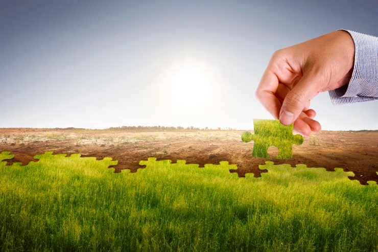 A hand taking away a piece of grass puzzle leaving the land hollow and dried up.